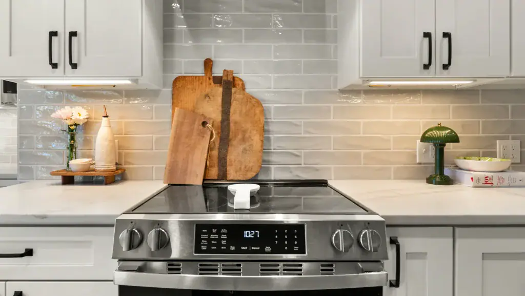 Stainless steel range beneath a hood, framed by white cabinets and a pale tile backsplash.