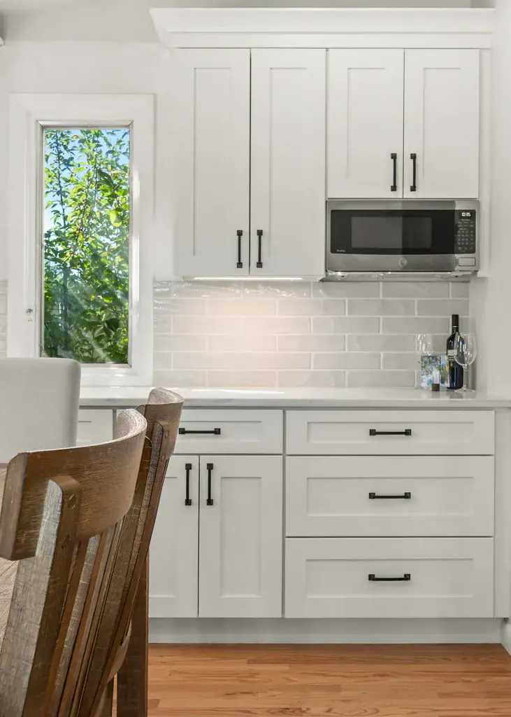 Tall white cabinetry with black hardware, an integrated microwave, and a narrow window.