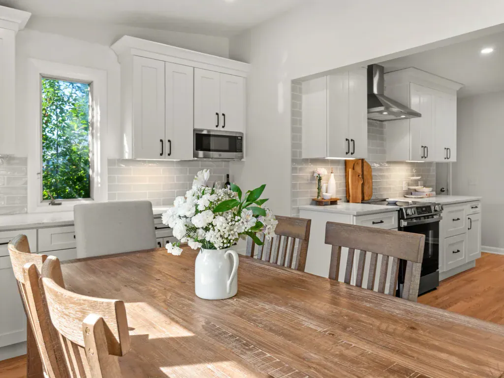 Wood dining table with flowers overlooking the white kitchen, range, and oak island.