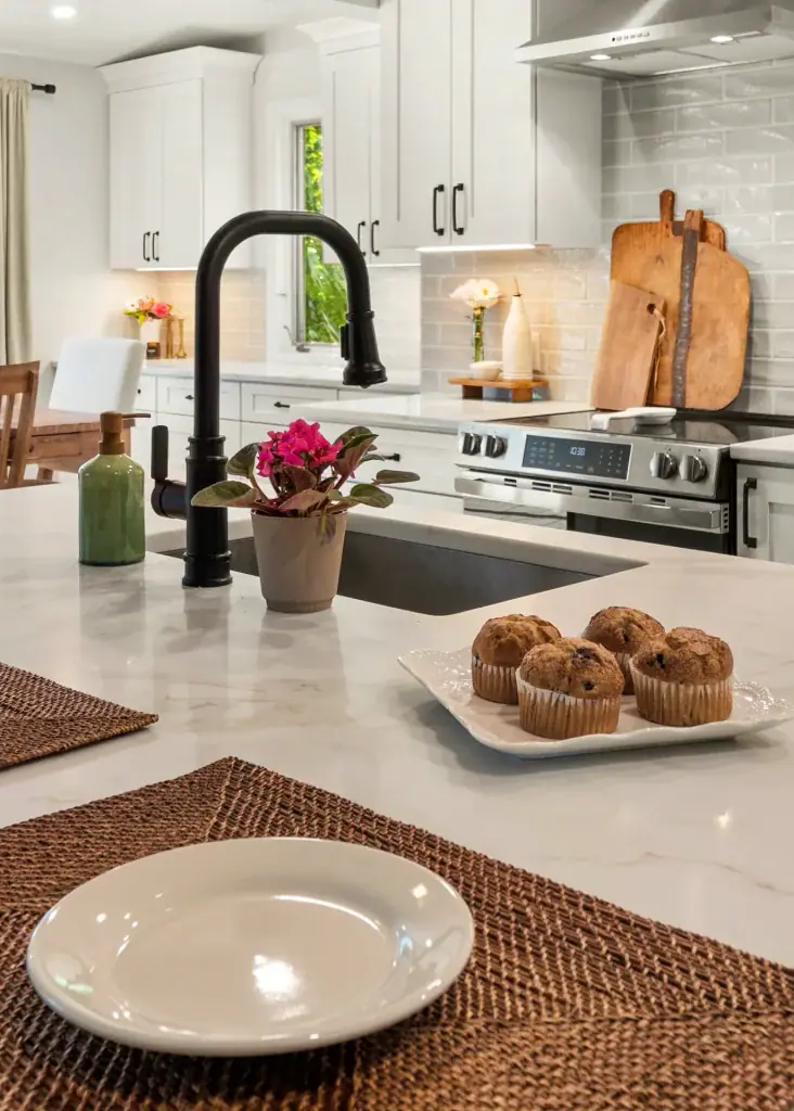 Place setting and muffins on the quartz island with the black faucet and white kitchen beyond.